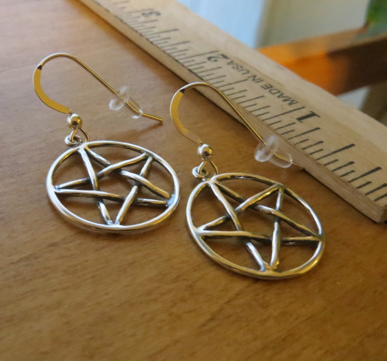 May include: A pair of silver earrings featuring a pentagram design. The earrings are made from sterling silver and have a simple, elegant design.