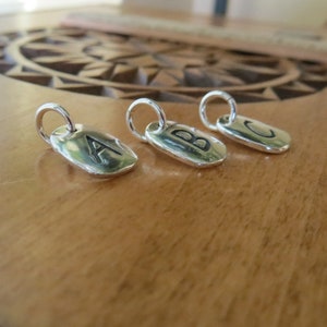 Puede incluir: Tres abalorios de plata con las letras A, B y C grabadas en ellos. Los abalorios son de forma ovalada y tienen un bucle en la parte superior para sujetarlos a un collar o pulsera.