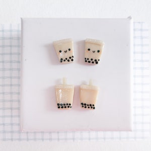 May include: Four handmade polymer clay earrings shaped like boba tea cups with black dots and a smiling face.