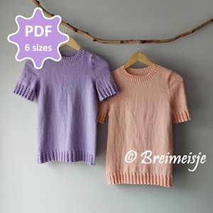 Op de afbeelding: Twee gebreide shirts met korte mouwen, één lavendelkleurig en één perzik, hangen aan houten hangers. De shirts hebben geribbelde manchetten en zomen. Een tak en de tekst "PDF 6 sizes" zijn zichtbaar.