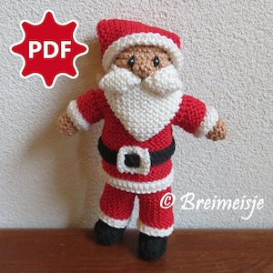 Op de afbeelding: Een handgemaakte gebreide kerstmanpop in rood, wit, zwart en bruin. De pop heeft een witte baard, een zwarte riem met een witte gesp en een rode muts. De afbeelding bevat de tekst "PDF" en de naam "Breimeisje".