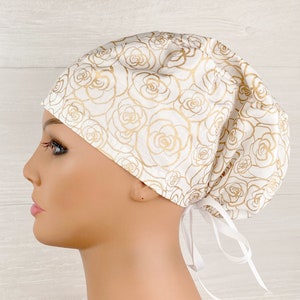 May include: White scrub hat with a gold floral pattern. The hat has a tie at the back.