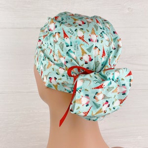 May include: A turquoise blue scrub hat with a pattern of gnomes and Christmas trees. The hat has a red tie that is tied in a bow at the back.