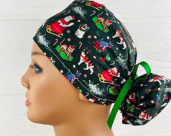 May include: A dark green scrub cap with a Christmas cat pattern. The fabric displays cats dressed as Santa, reindeer, and elves, alongside candy canes and Christmas trees. A green ribbon is tied at the back.
