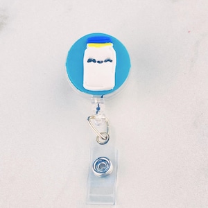 May include: A blue and white mason jar with a yellow lid, on a retractable badge holder. The mason jar has a black eye design.