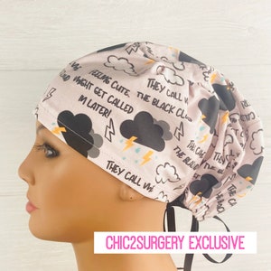 May include: A light pink scrub cap featuring a repeating pattern of black storm clouds, yellow lightning bolts, and blue raindrops. The fabric includes printed text that reads, "FEELING CUTE. MIGHT GET CALLED IN LATER!" and "THEY CALL ME THE BLACK CLOUD."