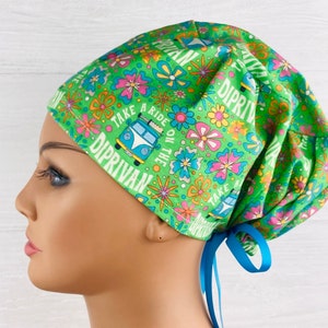 May include: Green scrub hat with a colourful floral pattern and a vintage van graphic. The hat has the text "Take a ride on the DipRivan" printed on it. The hat has blue ties.