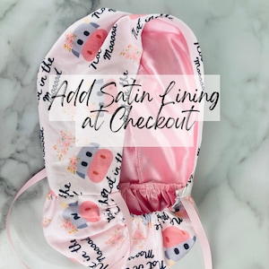Puede incluir: Un gorro rosa y blanco con un estampado de vaca en el exterior y un forro de sat&eacute;n rosa. El gorro tiene un cord&oacute;n y el texto "Not in the mood" y "Mooooa" est&aacute; impreso en el exterior. El texto "Add Satin Lining at Checkout" tambi&eacute;n es visible.