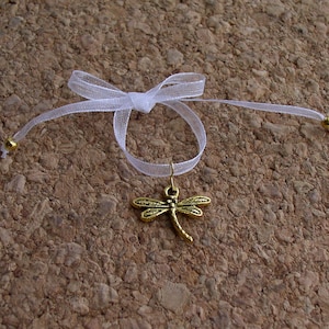 Peut inclure: Un ruban blanc noué en un nœud avec un charme de libellule dorée suspendu.