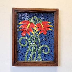 Könnte beinhalten: Ein gerahmtes Keramikfliesenmosaik mit zwei stilisierten roten und gelben Blumen mit grünen Ranken auf blauem Hintergrund mit weißen Punkten.