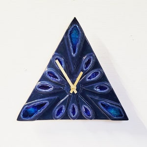 May include: A triangular blue ceramic clock with gold hands and a geometric design. The clock face is a dark blue with a lighter blue pattern.