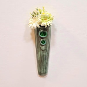 May include: A white ceramic mug with a black handle and the text "But First, Coffee" in a bold, black font. The mug is set against a blurred background, suggesting a cosy setting.