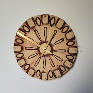 May include: A round ceramic wall clock with a brown and white design. The clock has gold hands and a simple design.
