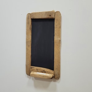 May include: A rectangular chalkboard with a black surface, framed by weathered, light brown wooden planks. A piece of white chalk rests at the bottom. The chalkboard is designed for writing or drawing.