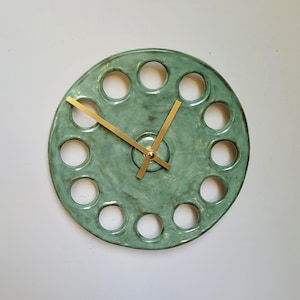 May include: A green ceramic clock with gold hands and a circular design featuring 12 evenly spaced holes.