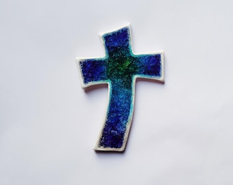 Könnte beinhalten: Ein blaues und grünes Glaskreuz mit weißem Rand. Das Kreuz besteht aus kleinen Glassplittern, die miteinander verschmolzen sind.