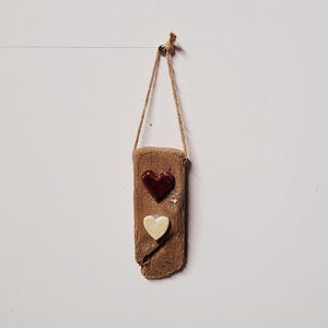 May include: A rustic wooden sign with a brown heart and a white heart, hanging from a twine rope.