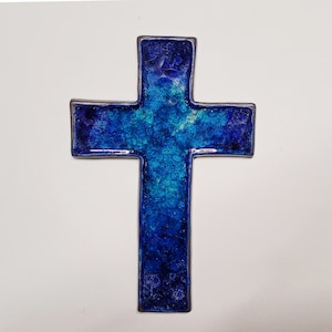 Puede incluir: Una cruz decorativa con un diseño tipo mosaico. La cruz presenta un degradado de azules, desde el índigo profundo hasta el turquesa claro, con una apariencia texturizada y agrietada. Los bordes están delineados con un borde metálico oscuro.