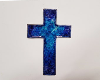 Könnte beinhalten: Ein dekoratives Kreuz mit einem mosaikartigen Design. Das Kreuz weist einen Farbverlauf von Blau auf, von tiefem Indigo bis zu hellem Türkis, mit einer strukturierten, rissigen Optik. Die Ränder sind von einer dunklen, metallischen Umrandung umgeben.