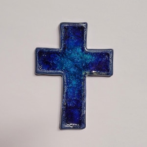 May include: A blue glass cross with a textured surface. The cross is made of small pieces of glass that have been fused together.