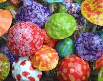 May include: A collection of ceramic mushroom sculptures featuring glossy, rounded caps in a vibrant array of colors including red, purple, lime green, orange, yellow, and blue, each decorated with distinct spotted or marbled patterns.