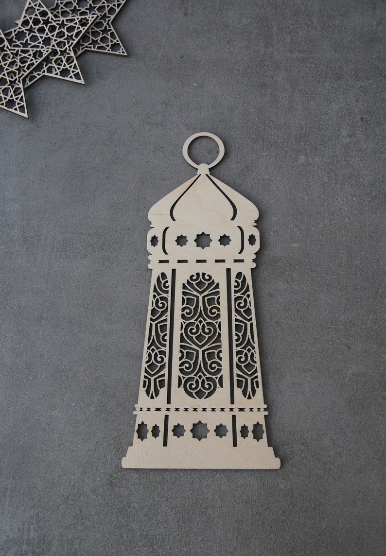 May include: A wooden cutout of a decorative lantern with intricate designs. The lantern is light brown and has a traditional Islamic style.