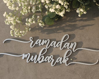 Op de afbeelding: Een zilveren glitter Ramadan Mubarak-bord met een cursief lettertype. Het bord is gemaakt van hout en perfect om te decoreren voor de islamitische feestdag.