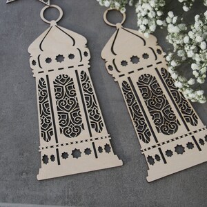 May include: Two wooden cutout lanterns with intricate designs. The lanterns are light brown and have a traditional Moroccan style.