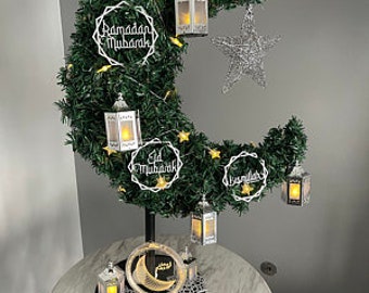May include: A crescent moon-shaped green floral arrangement with a star and lanterns. The arrangement has a metal stand and features Ramadan Mubarak, Eid Mubarak, and other Islamic greetings.