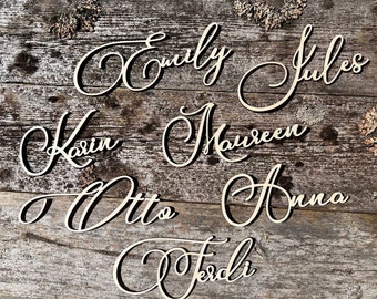May include: Seven wooden names, each with a cursive font, are displayed on a rustic wooden background. The names are: Emily, Jules, Karin, Maureen, Otto, Anna, and Jesdi.