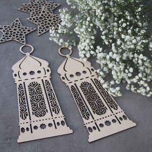 May include: Two wooden laser cut lanterns with intricate designs. The lanterns are light brown and have a traditional Moroccan style.