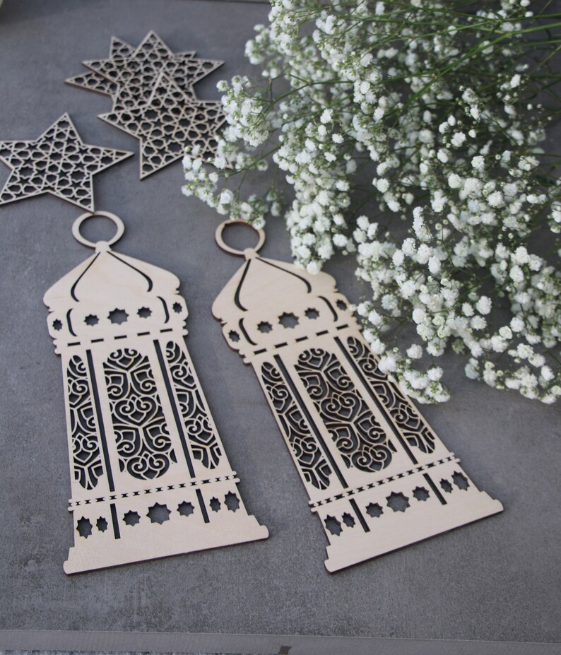May include: Two wooden laser cut lanterns with intricate designs. The lanterns are light brown and have a traditional Moroccan style.