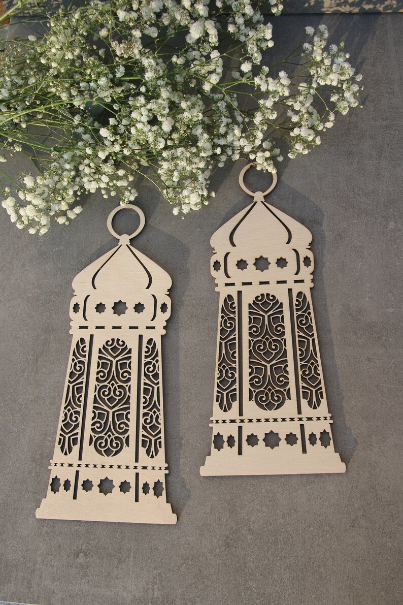 May include: Two wooden decorative lanterns with intricate cut-out designs. The lanterns are beige and have a traditional Islamic style.