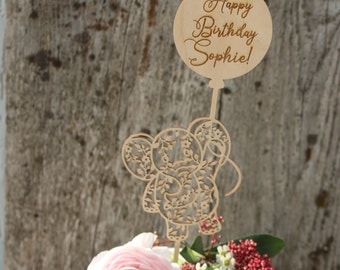 Può includere: Una torta bianca con fiori rosa e un topper per torta in legno. Il topper presenta un elefante floreale e un palloncino con il testo "Happy Birthday Sophie!"