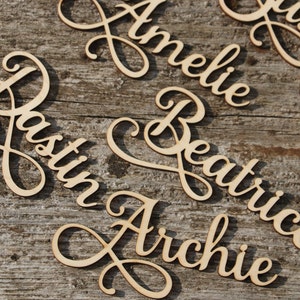 Puede incluir: Letreros de nombres de madera con letras cursivas. Los nombres son Dustin, Archie, Beatrice, Amelie y Gussie.