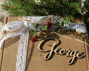 Puede incluir: Una caja de cartón marrón con una cinta de encaje blanco y cuerda. La caja está decorada con una etiqueta de madera con el nombre "George".