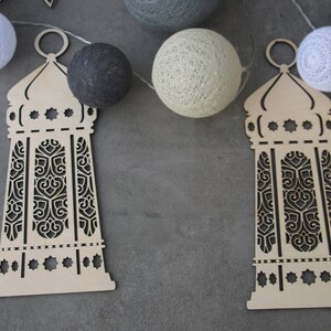 May include: Two wooden cutout lanterns with intricate designs, hanging from a string of white cotton balls. The lanterns are beige and have a dark brown intricate design.