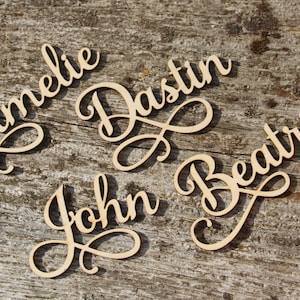 Puede incluir: Cuatro letreros de madera con nombres en letra cursiva. Los nombres son Amelia, Dustin, John y Beatrice.