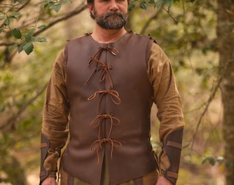 May include: A brown leather vest with a laced front, worn over a long-sleeved tan shirt. The vest has a simple design with leather ties. The sleeves have brown leather accents. The outfit is suitable for historical reenactment or costume events.