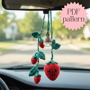 Könnte beinhalten: Ein handgefertigter Häkel-Autoanhänger mit Erdbeer-Design. Der Anhänger hat rote Erdbeeren mit grünen Blättern und Ranken sowie ein lächelndes Gesicht auf der größten Erdbeere. Der Text "PDF pattern" ist sichtbar.