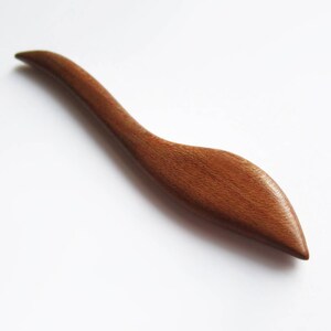 May include: A wooden hair stick with a curved, leaf-shaped design. The stick is a rich brown color and has a smooth, polished finish.