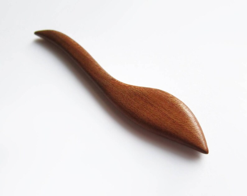 May include: A wooden hair stick with a curved, leaf-shaped design. The stick is a rich brown color and has a smooth, polished finish.