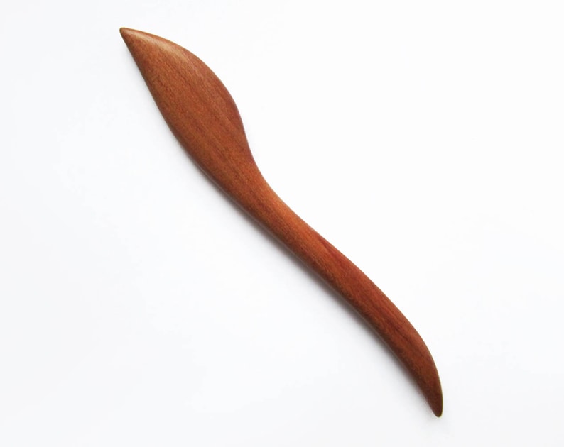 May include: A long, thin, wooden hair stick with a curved, leaf-shaped end. The stick is a reddish-brown color.