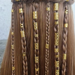Puede incluir: Primer plano de cabello castaño trenzado, adornado con cuentas doradas para el cabello. Las trenzas están decoradas con varias cuentas de metal dorado, agregando un elemento decorativo al peinado. El cabello está peinado en múltiples trenzas.
