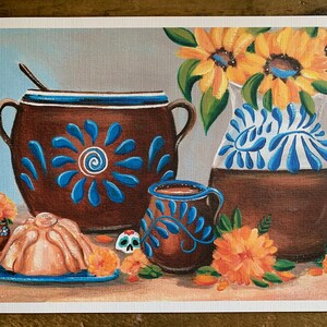 May include: A still life painting featuring a brown clay pot with blue and white floral designs, a smaller brown clay mug with blue and white floral designs, a light brown pan dulce, and a bouquet of yellow sunflowers in a brown clay pitcher with blue and white floral designs.