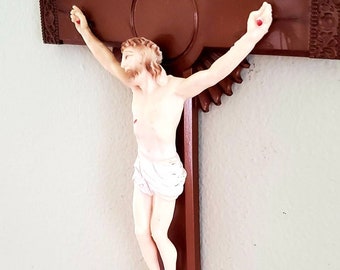 May include: A brown wooden crucifix with a white figure of Jesus Christ on it. The crucifix has a decorative design around the center and the words "INRI" on a white plaque above Jesus.