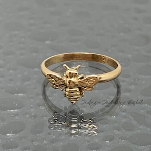 May include: A gold-toned ring featuring a three-dimensional bee ornament centered on the band. The bee has detailed wings and a segmented body. The text Judys Jewelry Basket is visible in the lower right corner of the image.