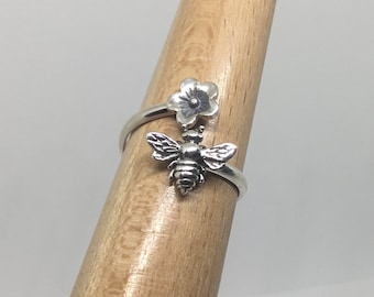 May include: A silver ring with a bee and flower design. The bee is detailed with wings and a body, and the flower is a simple five-petal design.