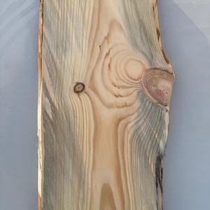 May include: A piece of natural wood with a light brown colour and a unique grain pattern. The wood has a rough, unfinished texture and a slightly irregular shape.