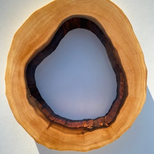 May include: A wooden slice with a large, irregular hole in the center. The wood is light brown with darker brown rings. The hole is surrounded by a dark brown border.